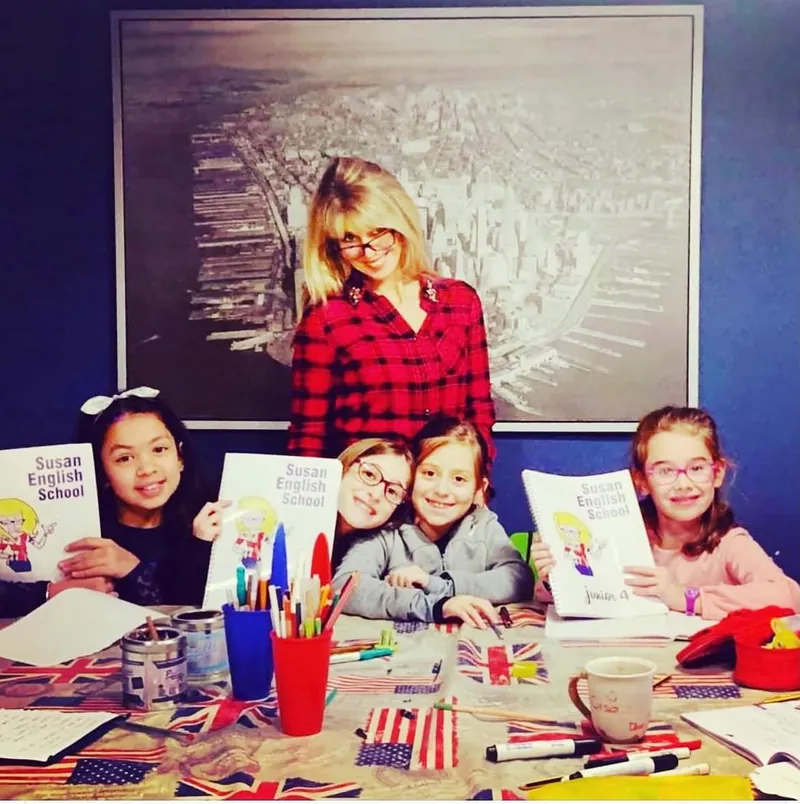 Un gruppo di bambine in classe mostra i quaderni della Susan English School insieme all'insegnante