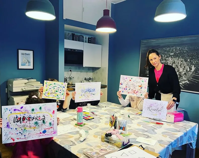 Bambini al tavolo mostrano i disegni colorati con i loro nomi durante un laboratorio