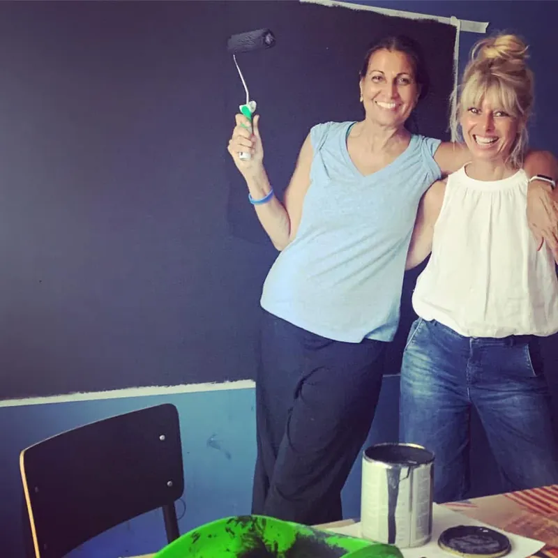 Due persone sorridenti dipingono di blu una parete della scuola